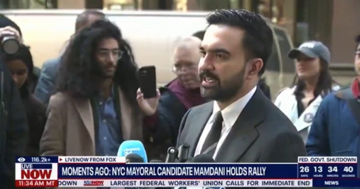 NYC mayoral candidate Mamdani speaks at a rally, surrounded by supporters and media, highlighting his campaign initiatives and engaging with the public.
