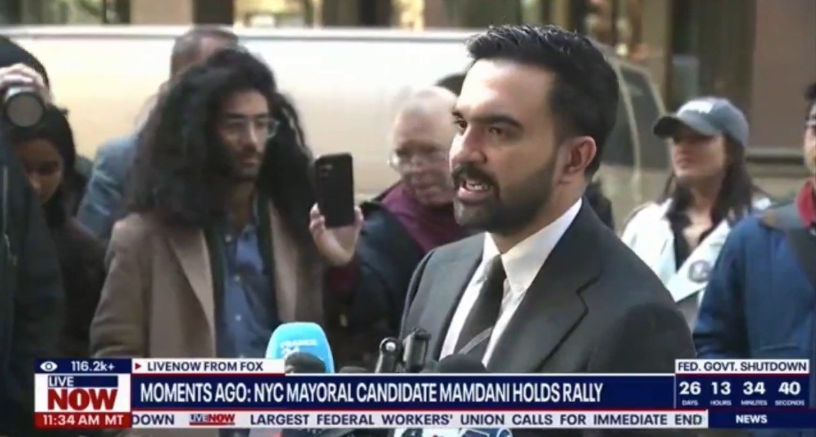 NYC mayoral candidate Mamdani speaks at a rally, surrounded by supporters and media, highlighting his campaign initiatives and engaging with the public.