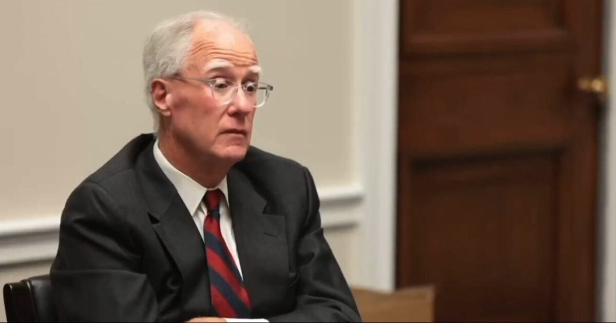 Business professional with glasses and a tie, engaged in a serious discussion during a meeting in an office setting.