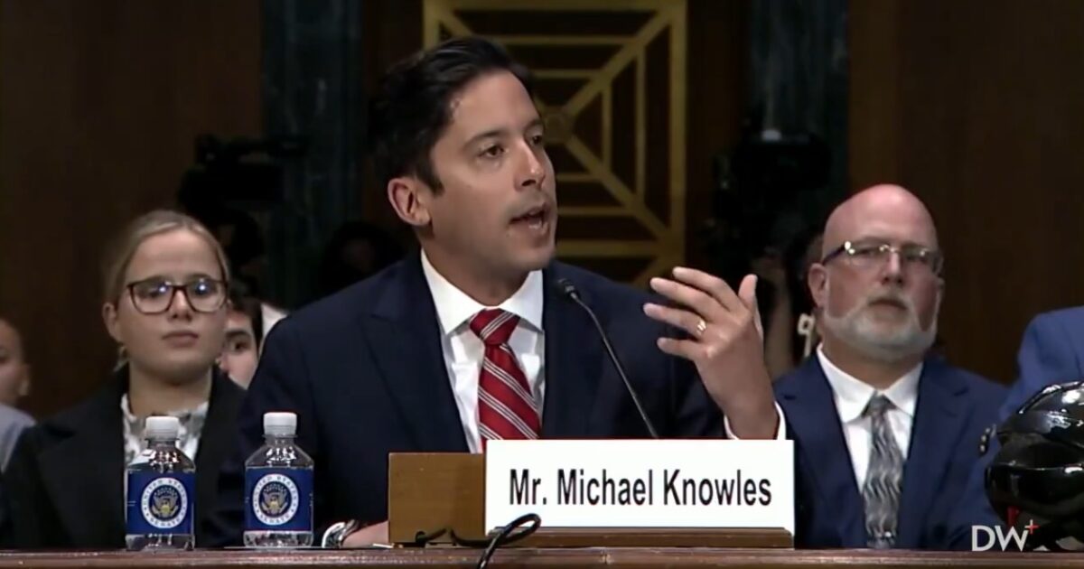 Michael Knowles testifies at a Senate hearing, discussing key issues while seated alongside other attendees, with water bottles and a nameplate visible.