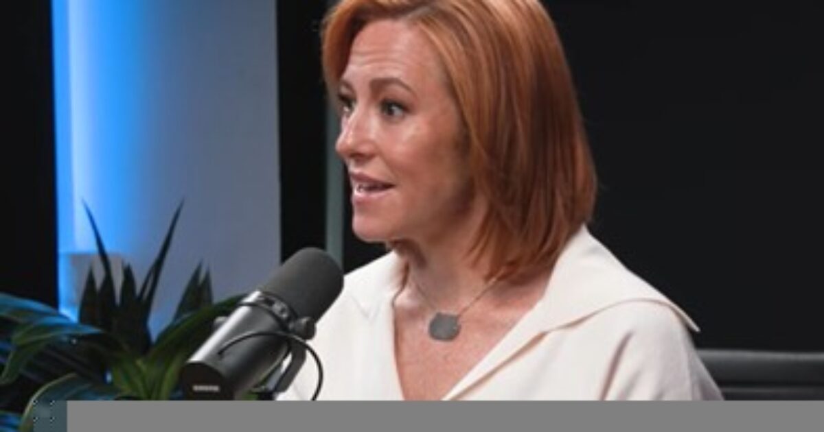 Woman with red hair speaking into a microphone during a podcast recording, surrounded by plants and modern decor.