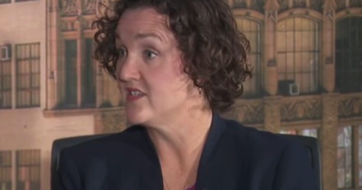 Woman with curly hair speaking in an interview setting, showcasing a professional demeanor against a backdrop of urban architecture.