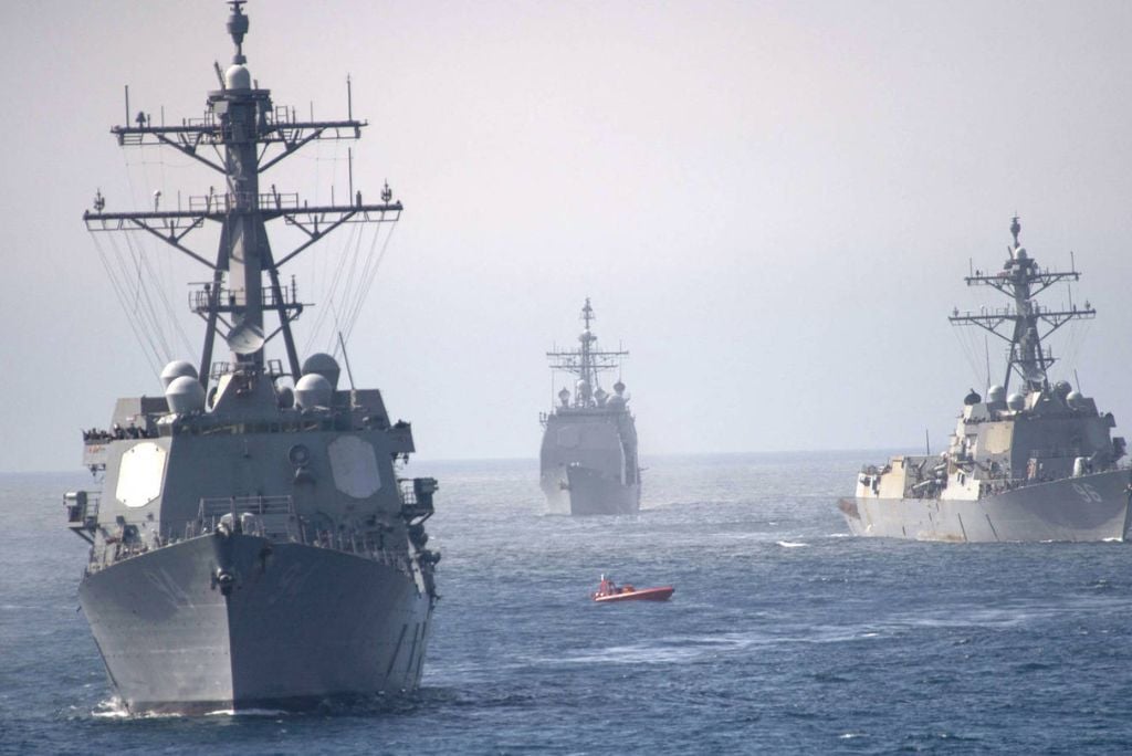 Three naval ships navigate through calm waters, accompanied by a small boat, showcasing maritime operations and naval strength.