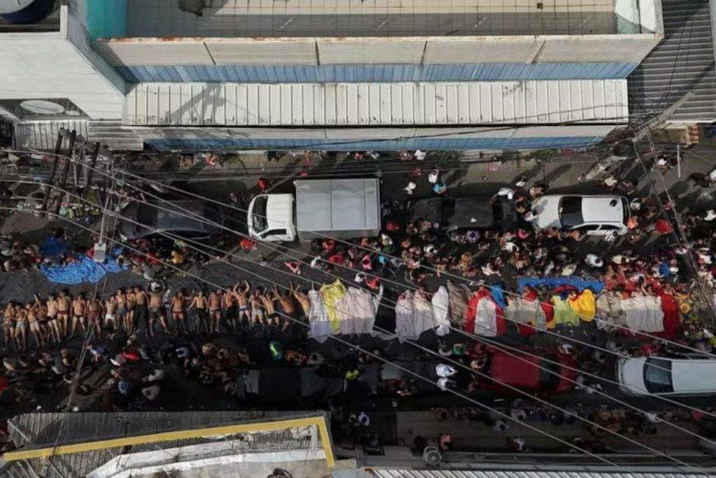 Aerial view of a crowded street scene with people lying on the ground and colorful fabrics, highlighting a significant public gathering or event.
