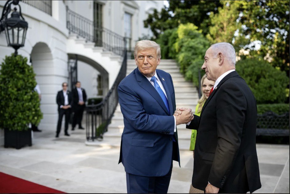 Donald Trump and Benjamin Netanyahu shake hands outside the White House, surrounded by greenery and security personnel, during a diplomatic meeting.