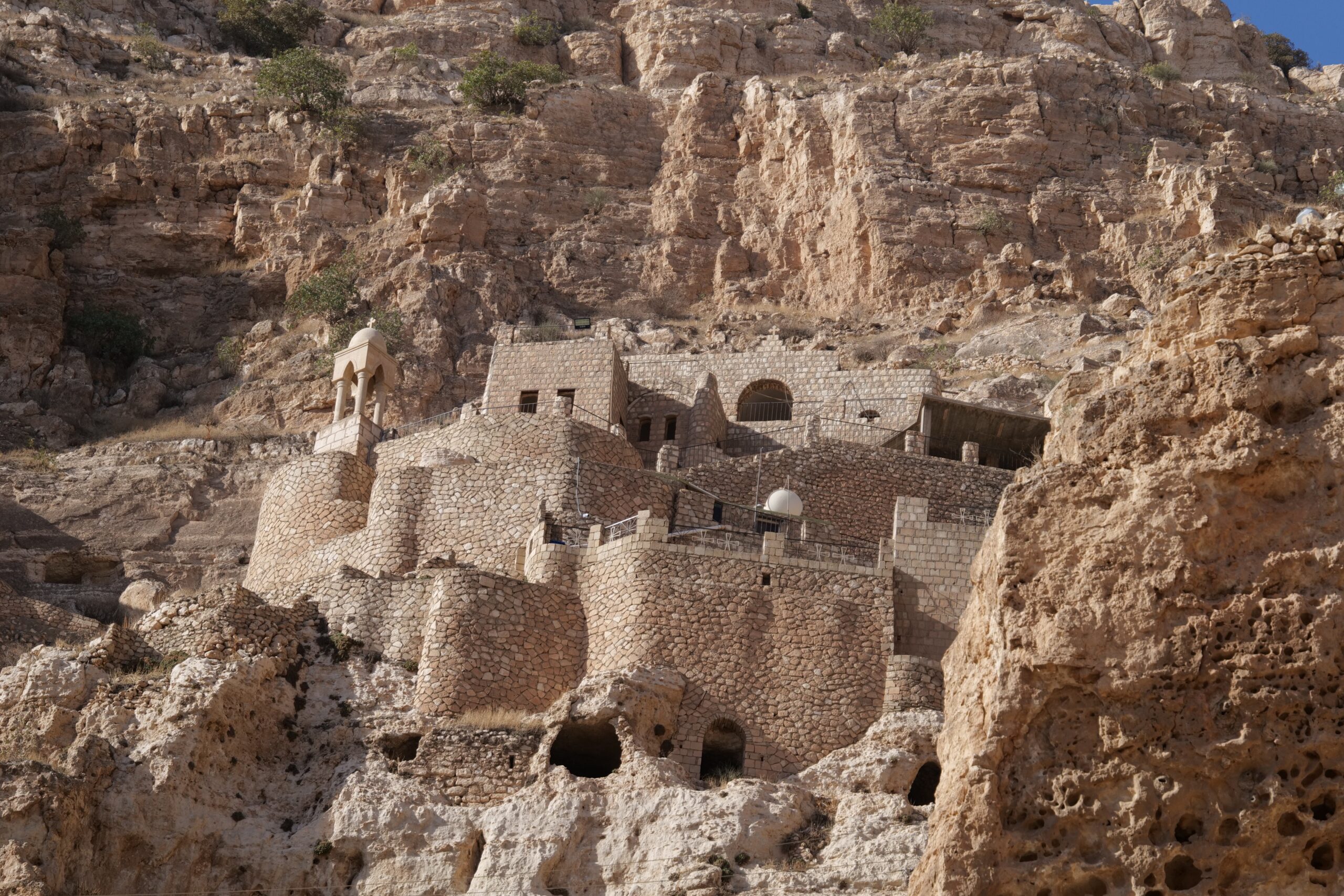 Ancient stone structures built into a rocky hillside, showcasing historical architecture and natural landscape in a desert environment.