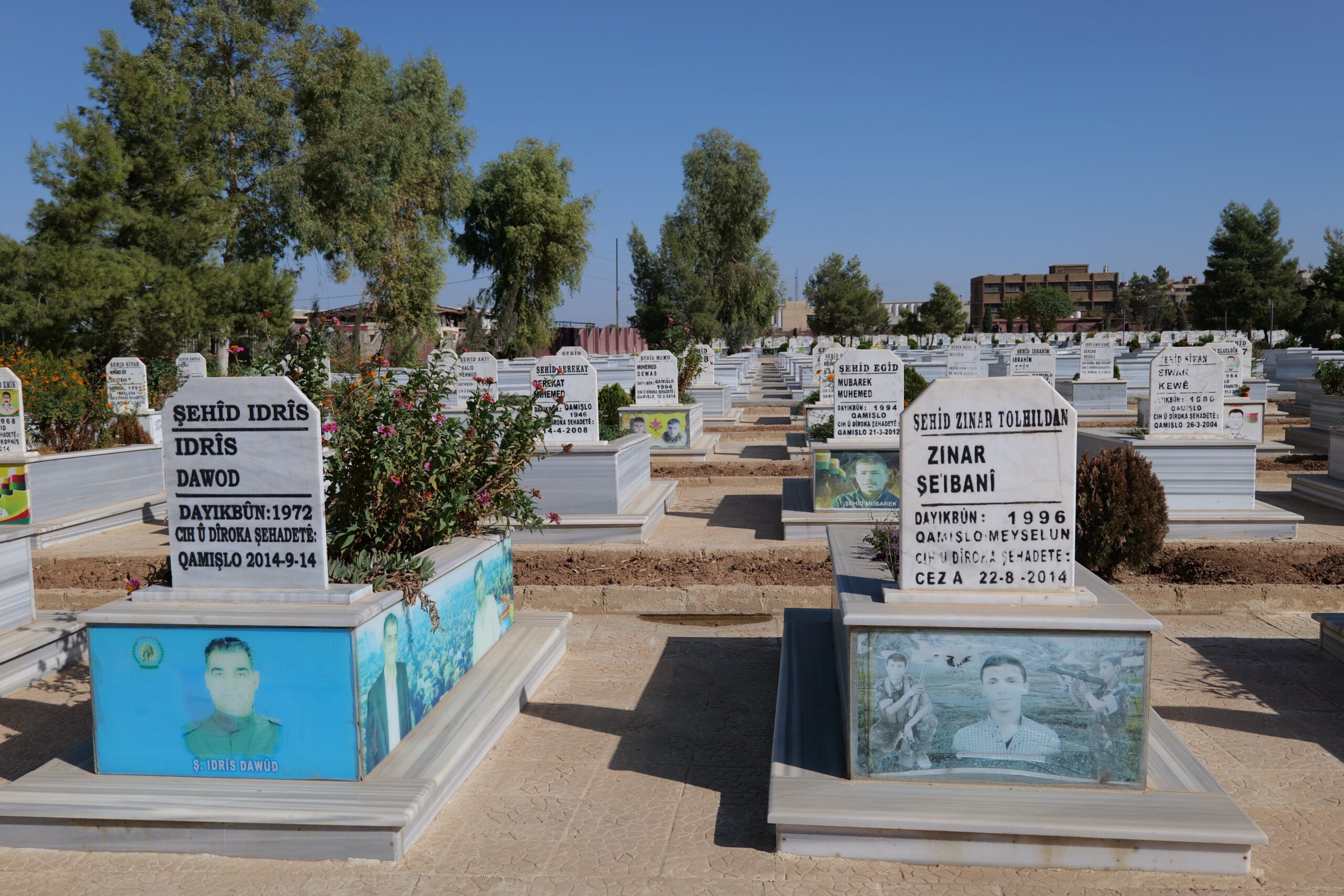 Graves of fallen soldiers in a cemetery featuring personalized headstones with photos, surrounded by greenery and flowers in a serene landscape.