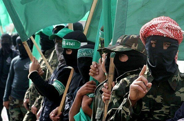 Masked individuals in military attire hold green flags during a demonstration, symbolizing their political affiliation and solidarity.