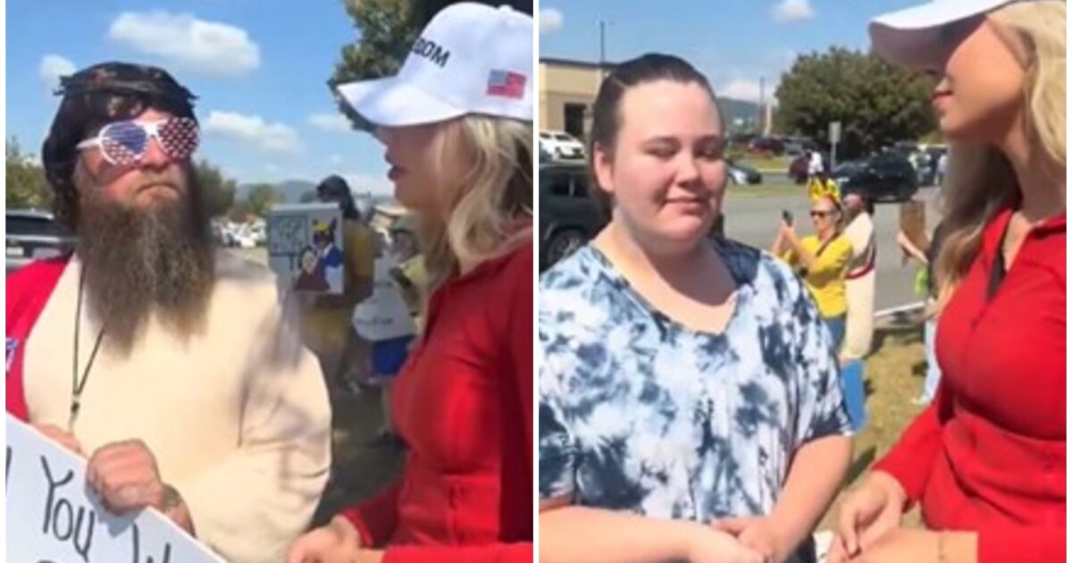 Two women engage in conversation at a public event, while a man with a beard and patriotic sunglasses holds a sign in the background.
