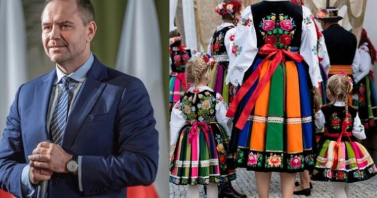 A man in a suit stands confidently next to women and children in colorful traditional Polish folk costumes at a cultural event.