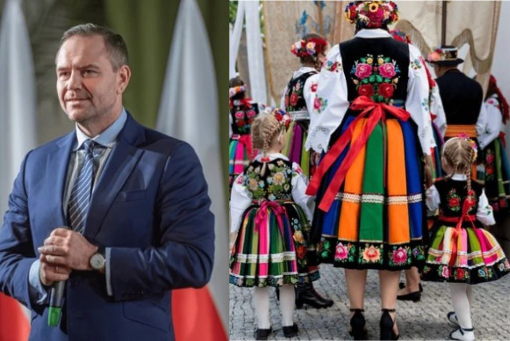A man in a suit stands confidently next to women and children in colorful traditional Polish folk costumes at a cultural event.