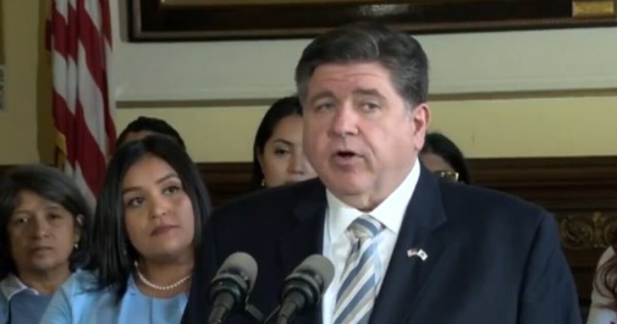 Illinois Governor J.B. Pritzker speaks at a press conference with supporters in the background, addressing key state initiatives and policies.