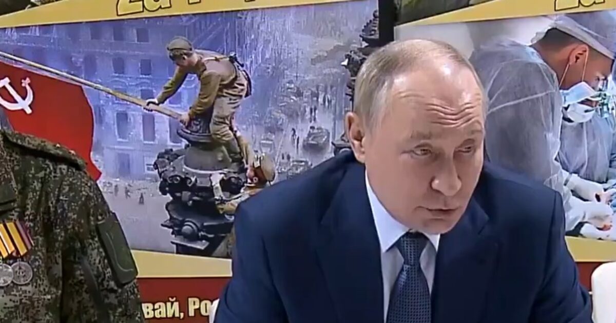 Russian leader Vladimir Putin speaking at a meeting, with military personnel and historical imagery in the background highlighting themes of patriotism and sacrifice.