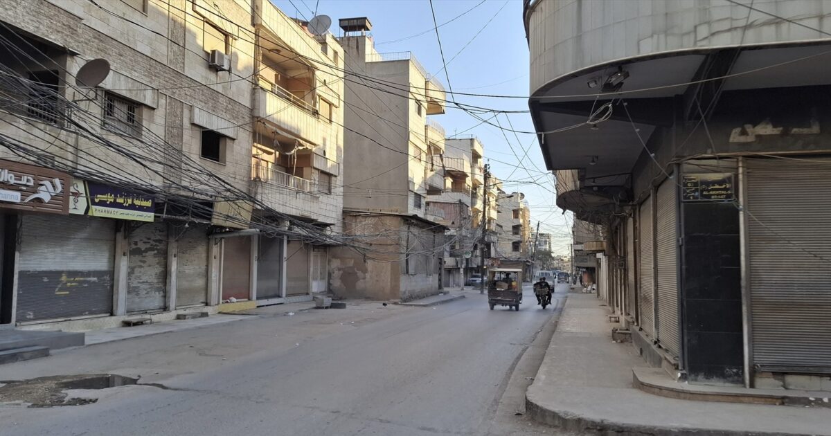 Empty street scene in an urban area with buildings, shops, and tangled overhead wires during daylight.
