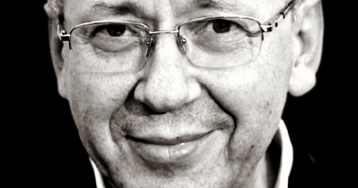Close-up portrait of a smiling middle-aged man with glasses, showcasing a friendly expression and subtle wrinkles in a black and white format.