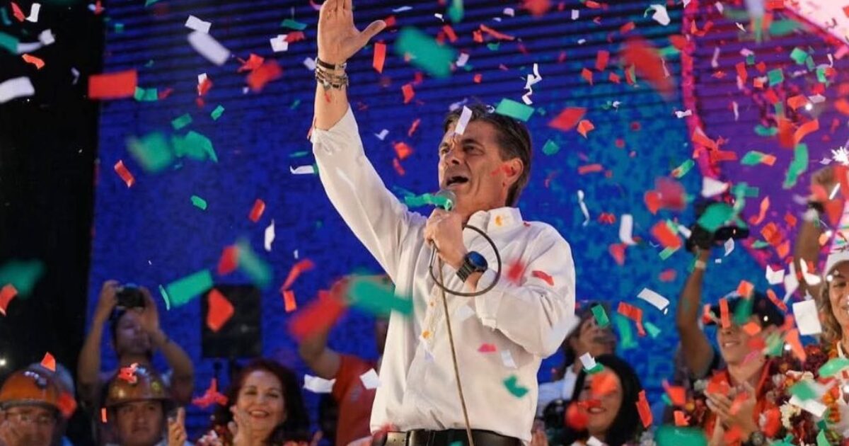 Political leader celebrates with confetti during a rally, engaging the crowd with a microphone in hand and a vibrant atmosphere.