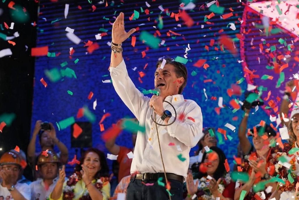 Political leader celebrates with confetti during a rally, engaging the crowd with a microphone in hand and a vibrant atmosphere.