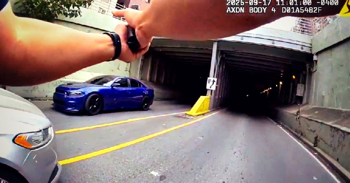 Police body camera footage capturing an officer pointing towards a dark tunnel with vehicles parked nearby.