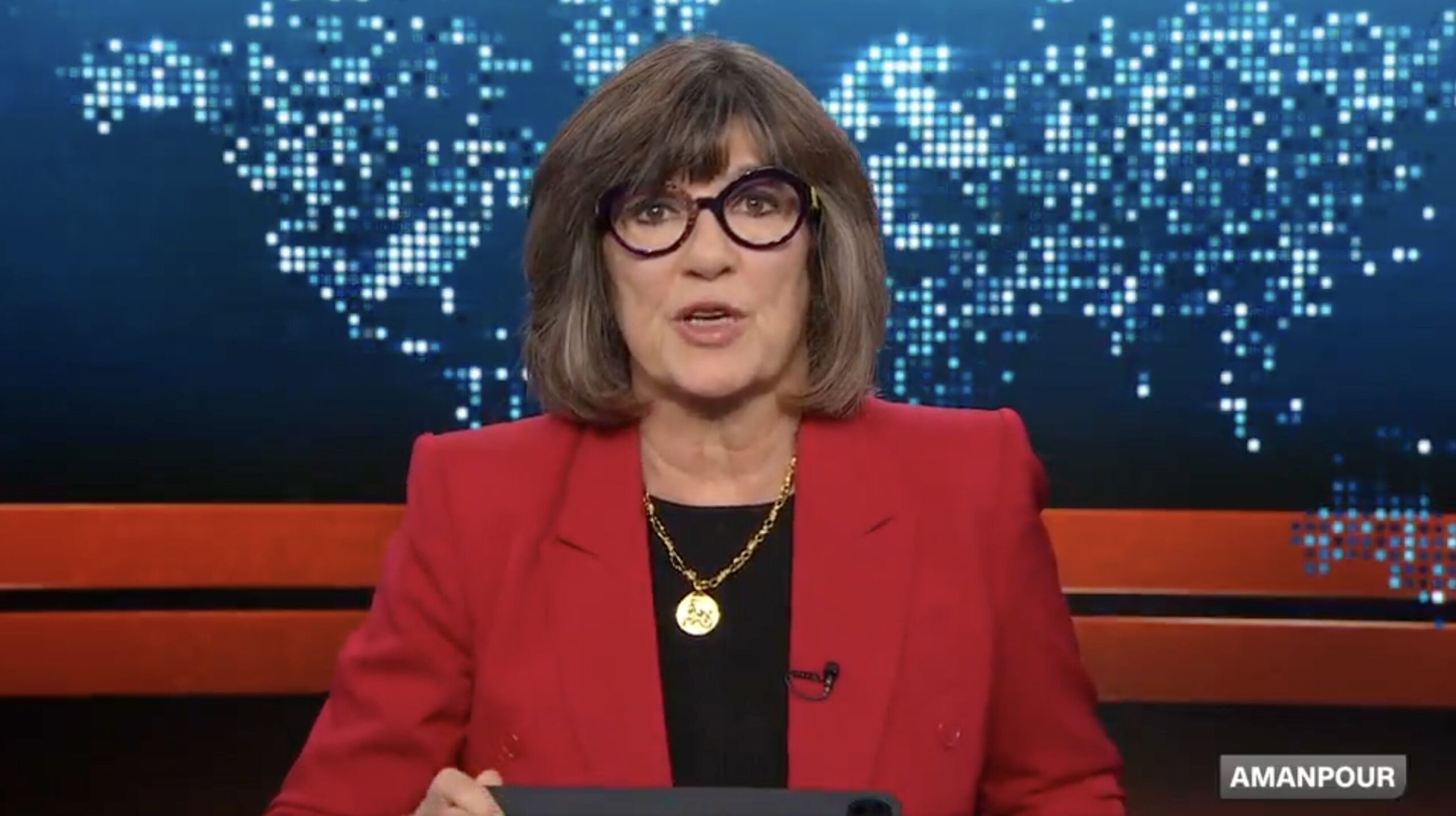 News anchor in a red blazer presents a segment against a digital world map background, highlighting current events and global issues.