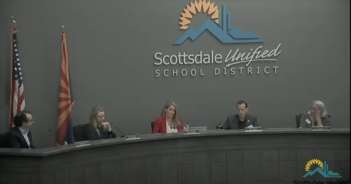 Scottsdale Unified School District board members discuss educational policies during a meeting, with flags displayed in the background.