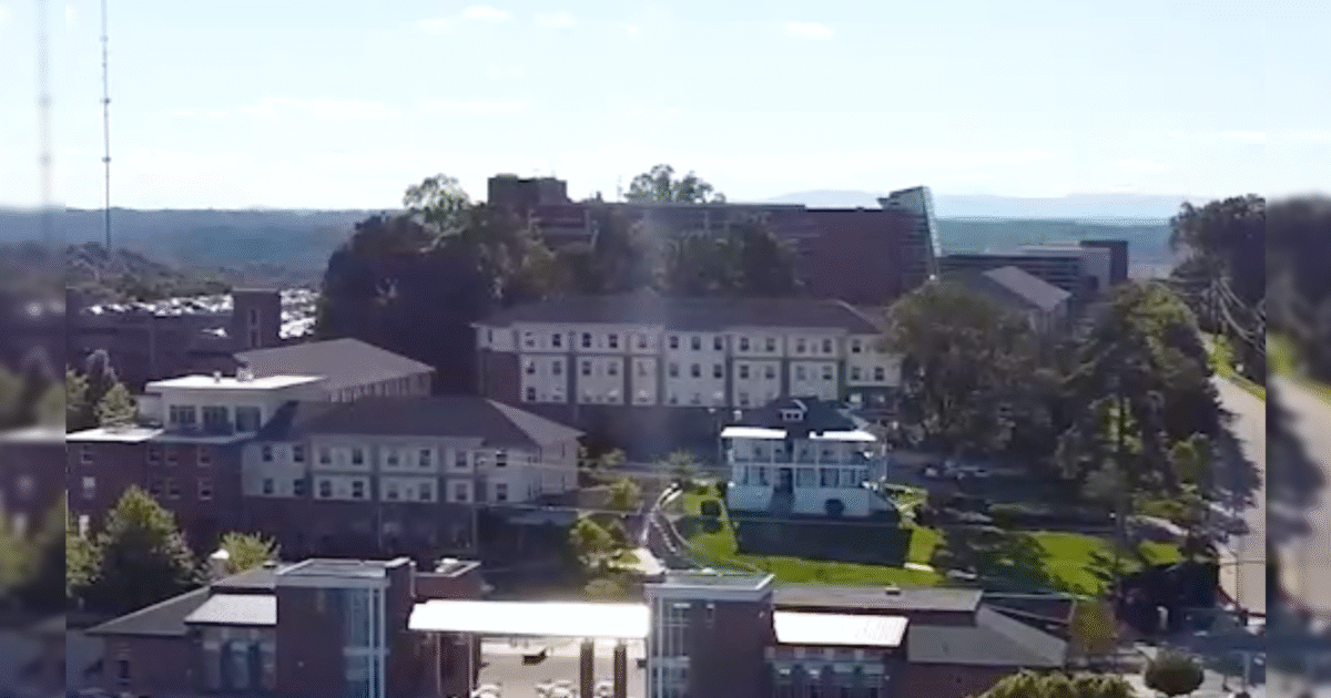Aerial view of a university campus featuring multiple buildings, green spaces, and a communication tower against a clear blue sky.