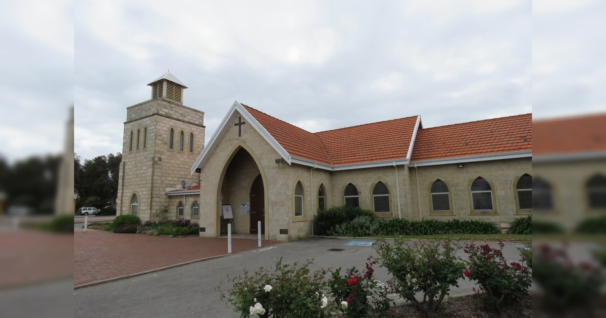 Historic stone church with a bell tower and arched windows, surrounded by landscaped gardens and colorful flowers.