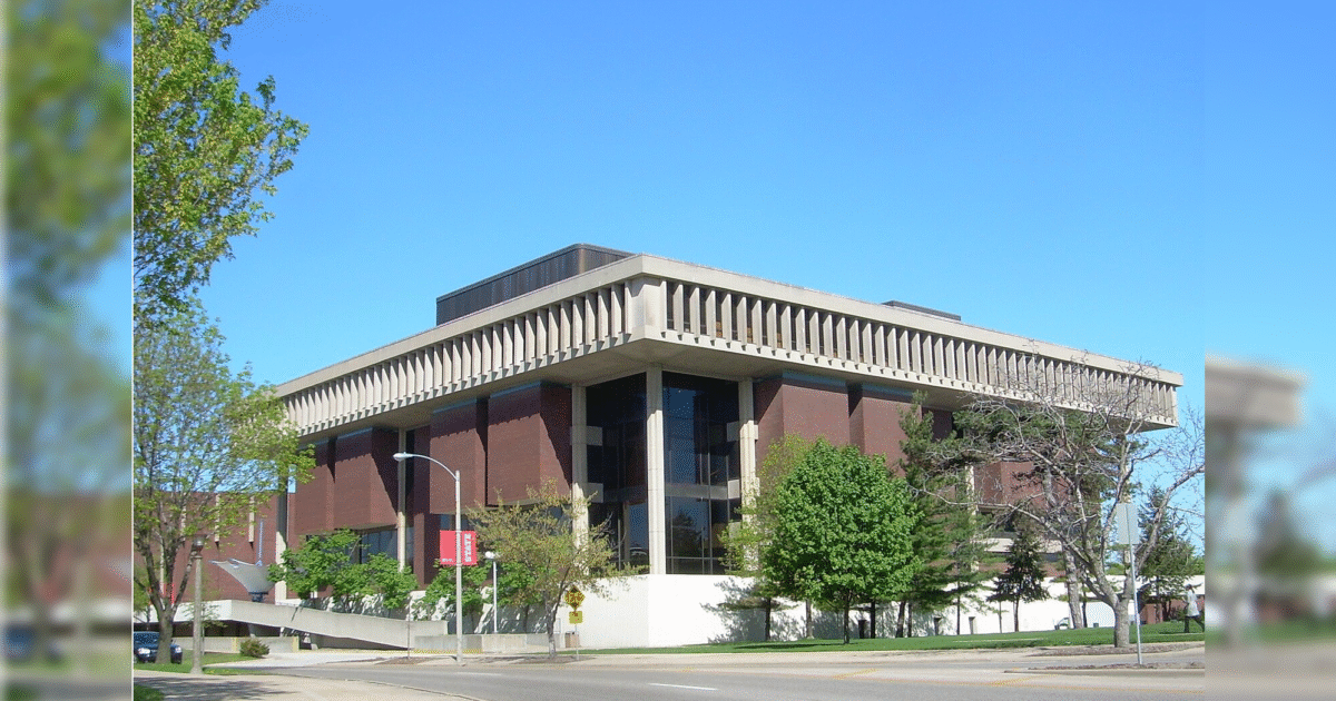 Modern architectural building with large glass windows surrounded by trees and clear blue sky, showcasing a blend of functionality and design.