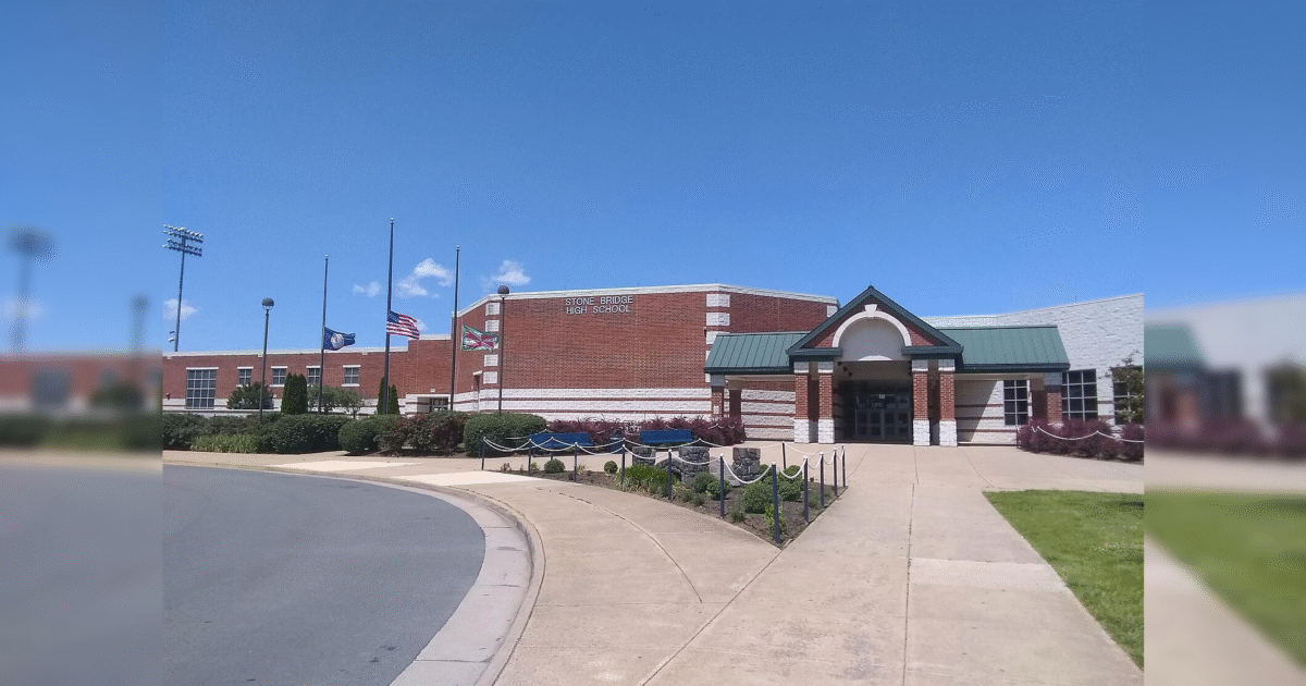 Exterior view of Stone Bridge High School featuring a brick facade, entrance, and landscaped grounds under a clear blue sky.