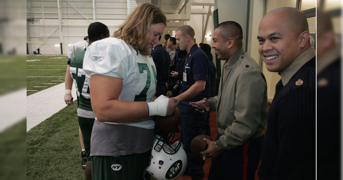 Football players interact with military personnel inside a practice facility, showcasing camaraderie and teamwork in sports.
