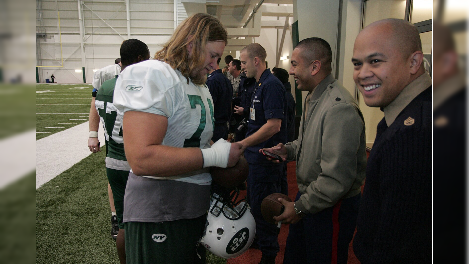New York Jets football players interact with military personnel during a team event in an indoor training facility.