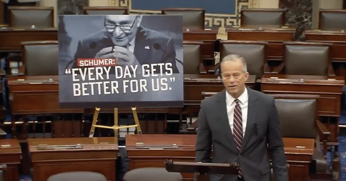 Senator John Thune speaks on the Senate floor with a large poster of Chuck Schumer in the background discussing positive progress.
