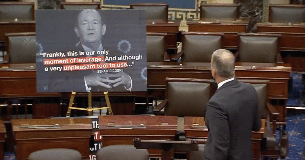 Senator Coons speaks in the Senate chamber, referencing a moment of leverage, with a large graphic displaying his quote in the background.