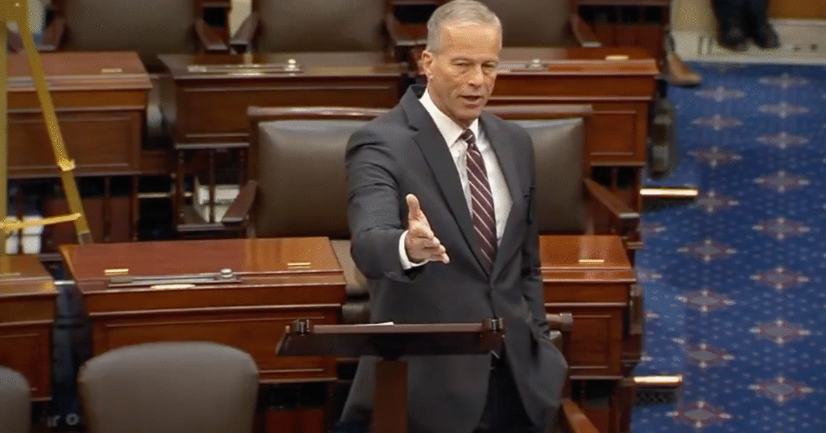 U.S. Senator speaking at a podium in the Senate chamber, addressing colleagues with a formal expression and gesturing during a session.