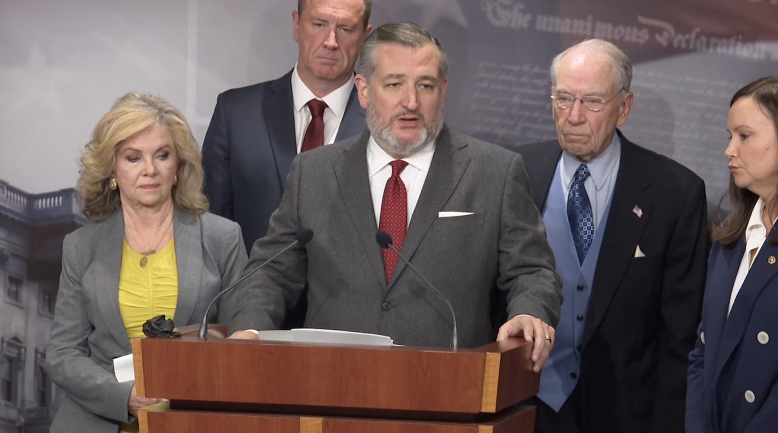Ted Cruz speaks at a press conference with fellow lawmakers, addressing key legislative issues, with a backdrop featuring historical documents.