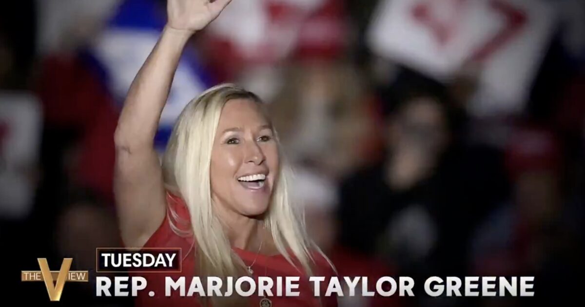 Rep. Marjorie Taylor Greene smiles and waves to a crowd during a political event, showcasing her engagement with supporters.
