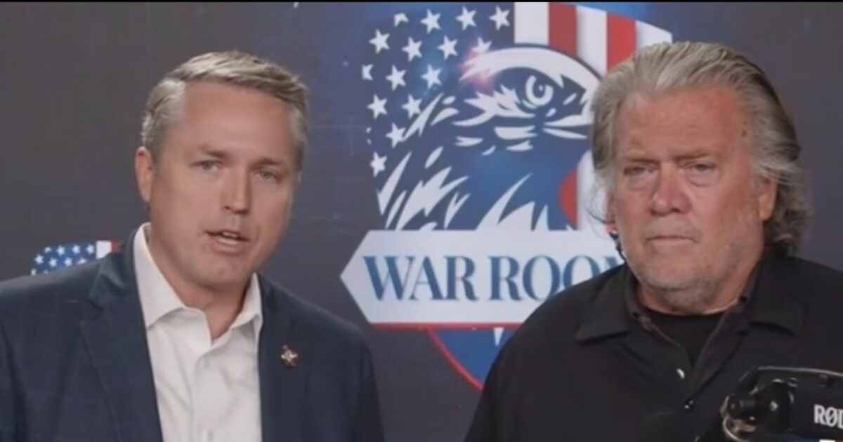 Two men speak in front of a "War Room" backdrop, discussing political topics and current events.