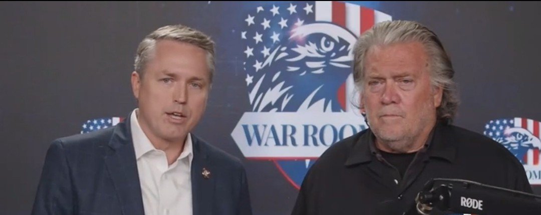 Two men speak in front of a "War Room" backdrop, discussing political topics and current events.