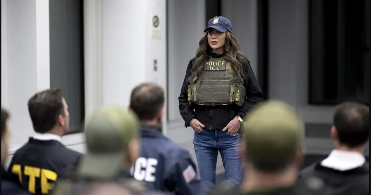A law enforcement officer in tactical gear addresses a group of agents during a training session in a modern facility.
