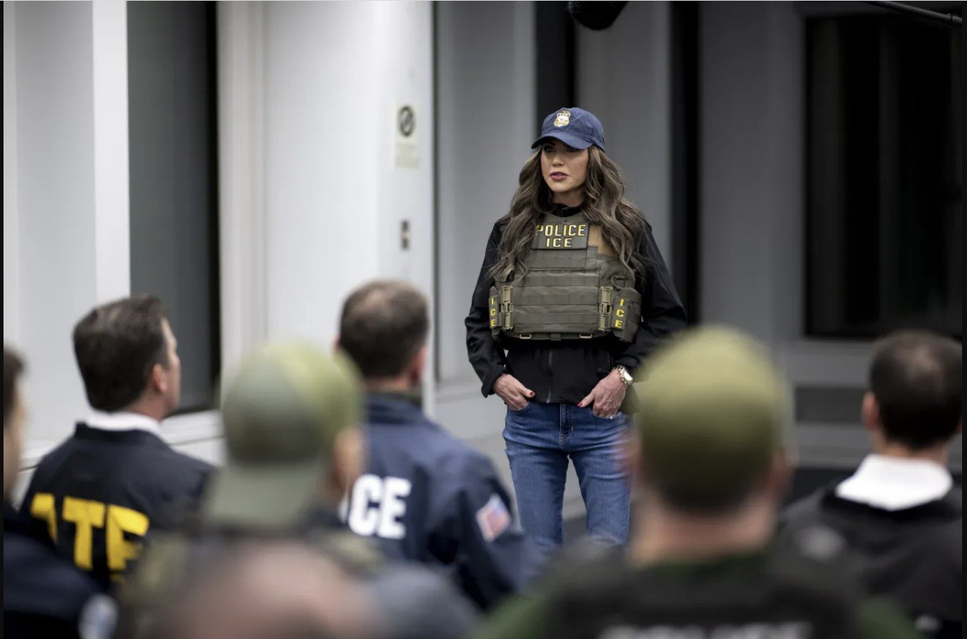 A law enforcement officer in tactical gear addresses a group of agents during a training session in a modern facility.