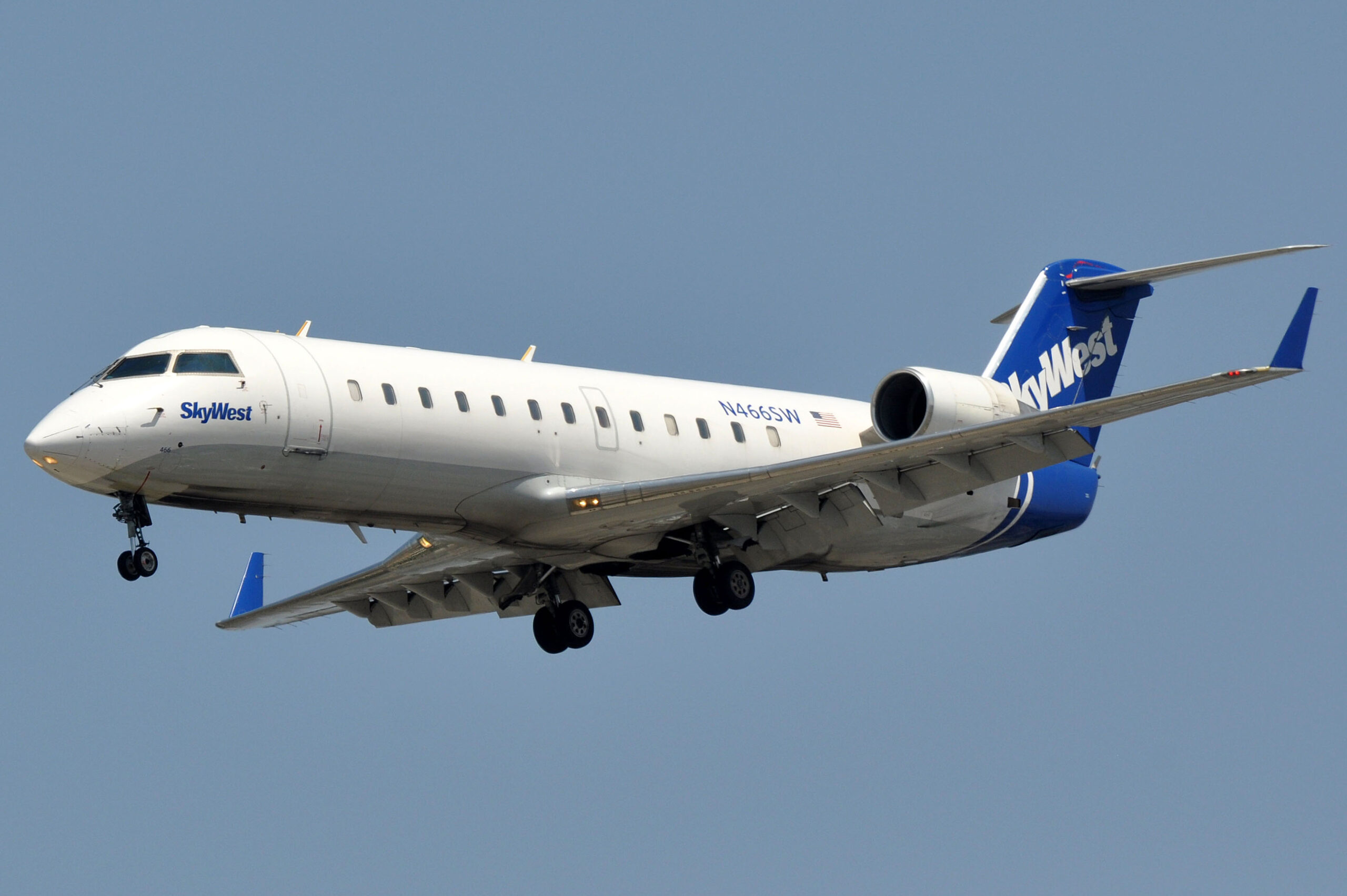 SkyWest Airlines regional jet approaching for landing against a clear blue sky.