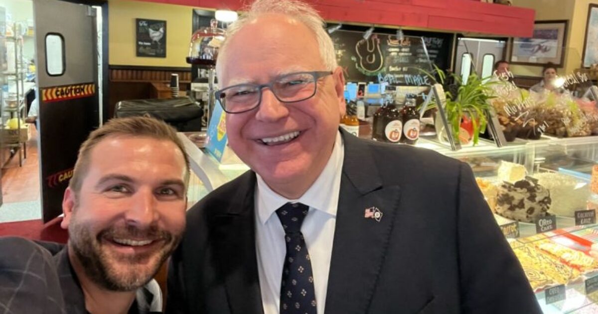 Selfie of two men smiling in a café with desserts in the background, showcasing a friendly atmosphere and community engagement.