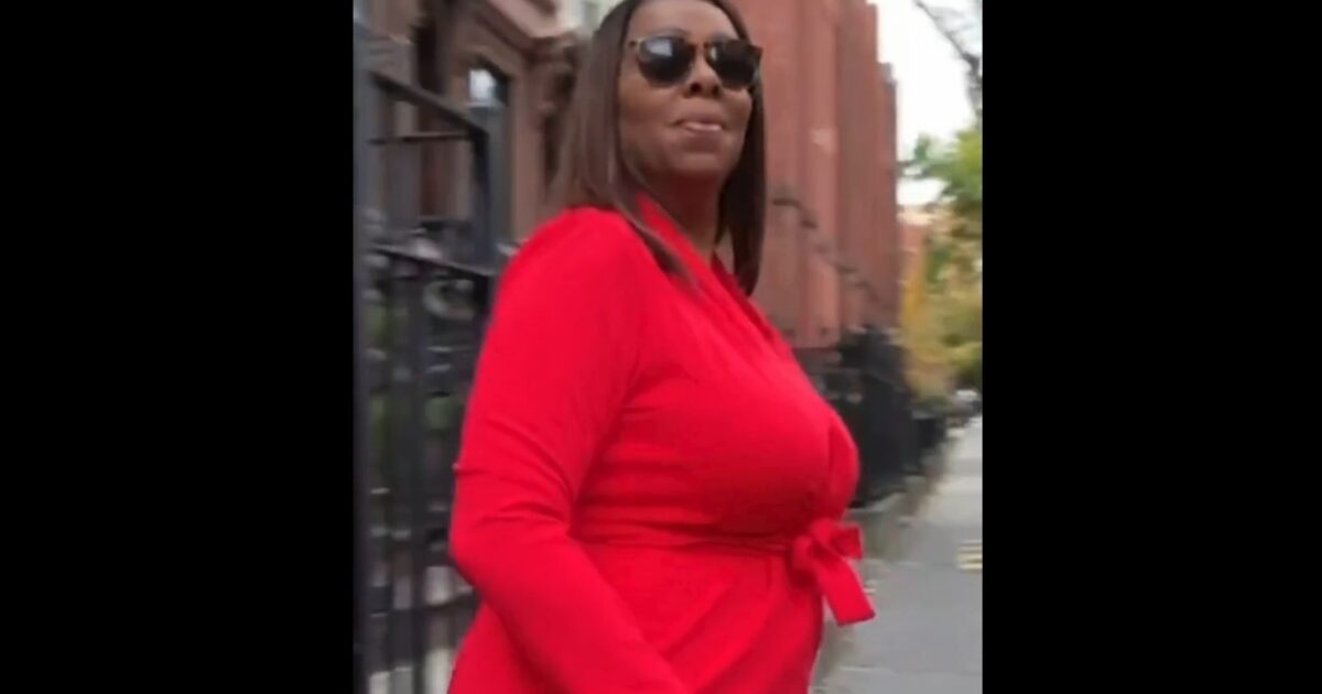 Woman in a red dress walking confidently on a city street, wearing sunglasses and smiling, with historic buildings in the background.