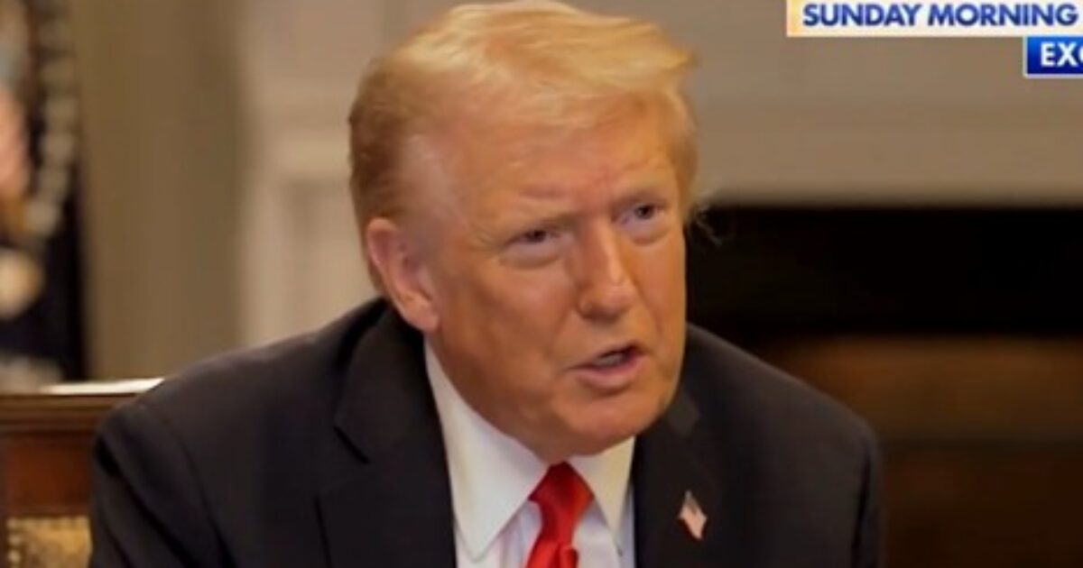 Donald Trump speaking in an interview setting, wearing a suit and tie, with a serious expression.