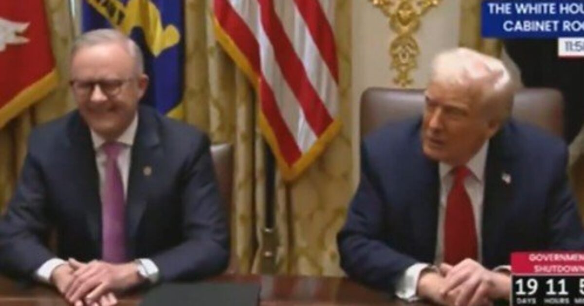 Two men seated at a table in the White House Cabinet Room, with flags in the background and a government shutdown countdown displayed.