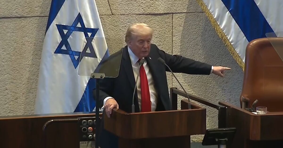 Donald Trump speaking at a podium in front of Israeli flags during a formal address.