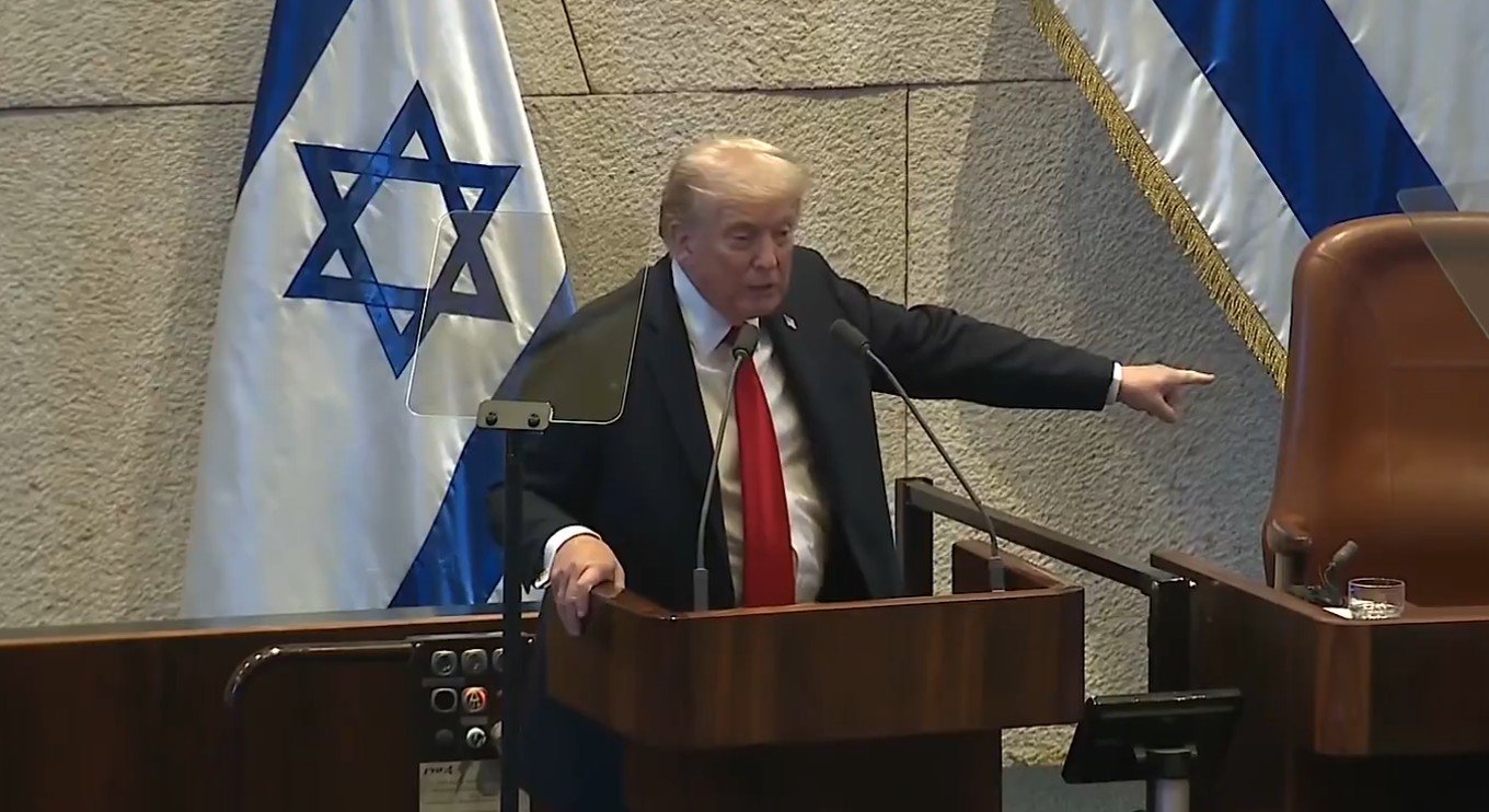 Donald Trump speaking at a podium in front of Israeli flags during a formal address.