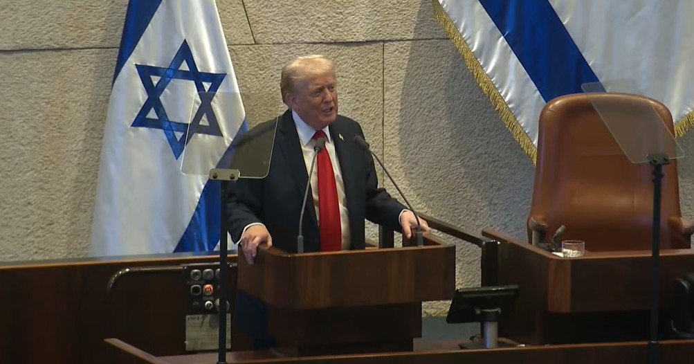 Donald Trump delivering a speech in front of the Israeli Knesset, with Israeli flags in the background.