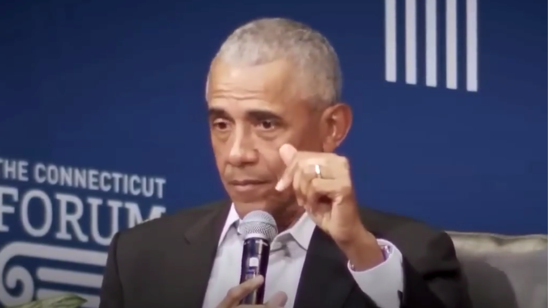 Barack Obama speaking at The Connecticut Forum, discussing key issues while holding a microphone and gesturing with his hand.