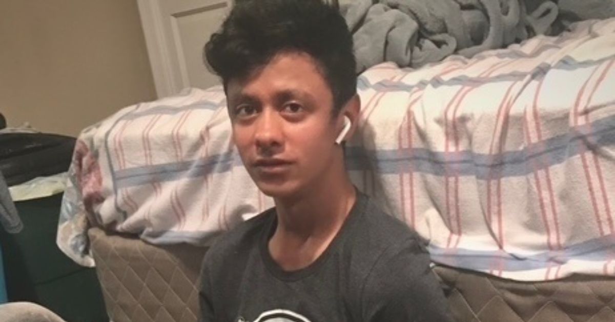Teenager sitting on the floor near a bed, wearing wireless earbuds and a casual t-shirt, with a relaxed expression in a cozy room setting.