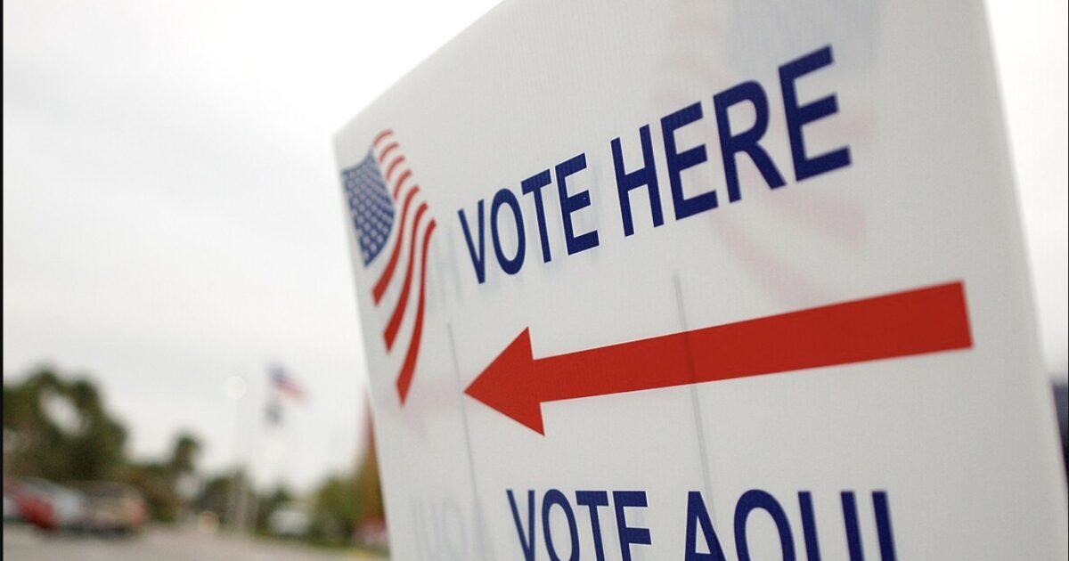 Voting sign directing individuals to the polling location with bilingual instructions in English and Spanish, featuring an American flag design.